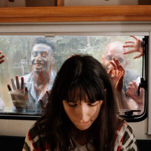 photo of girl in an rv while zombies pound on window behind her
